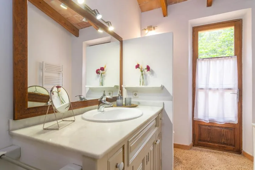 A bright bathroom vanity with a wide mirror and a curtained window.