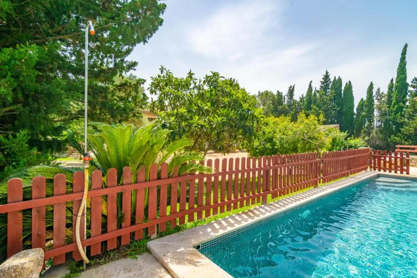 Outdoor swimming pool beside a red fence and lush greenery.