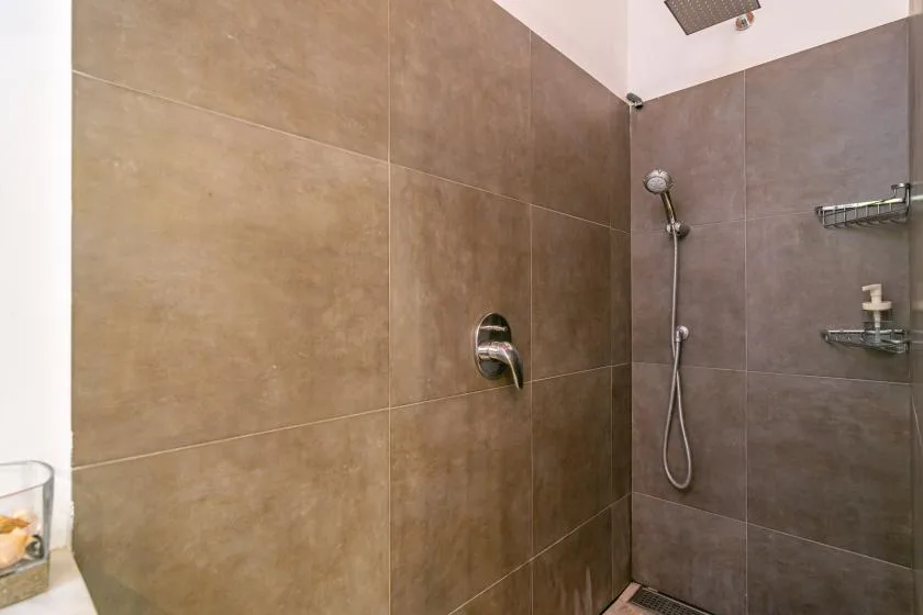A tiled shower area with a handheld showerhead and wall-mounted fixtures.