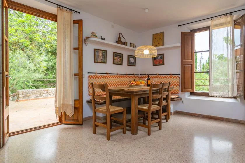 A dining area with a wooden table and chairs beside open windows.