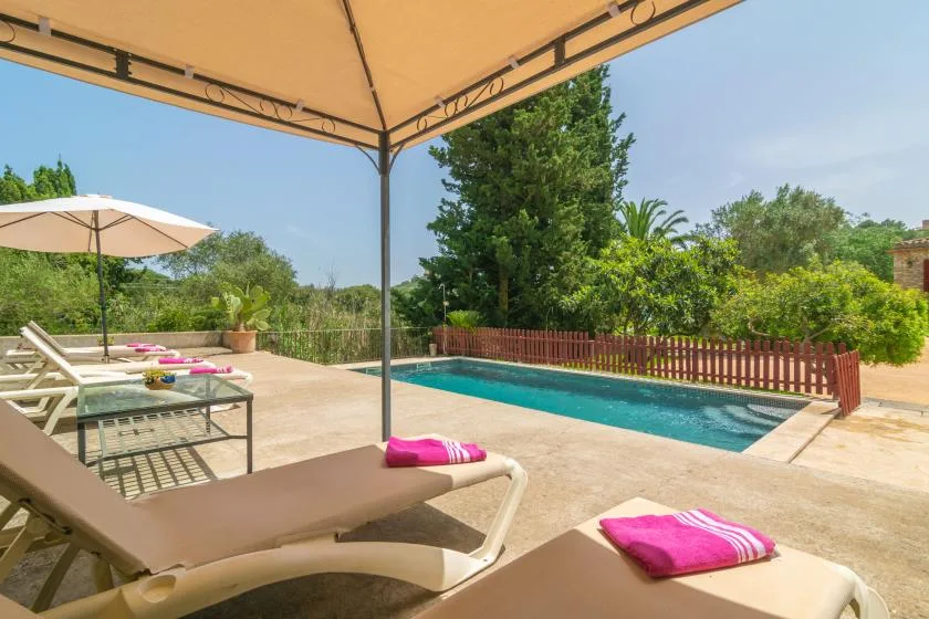 An outdoor swimming pool beside sun loungers under a large shade canopy.