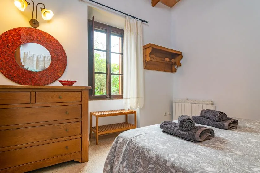 A bedroom with a wooden dresser, a window, and a bed with folded towels.
