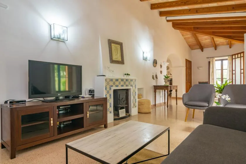 A living room with a television, tiled fireplace, seating, and exposed wooden ceiling beams.