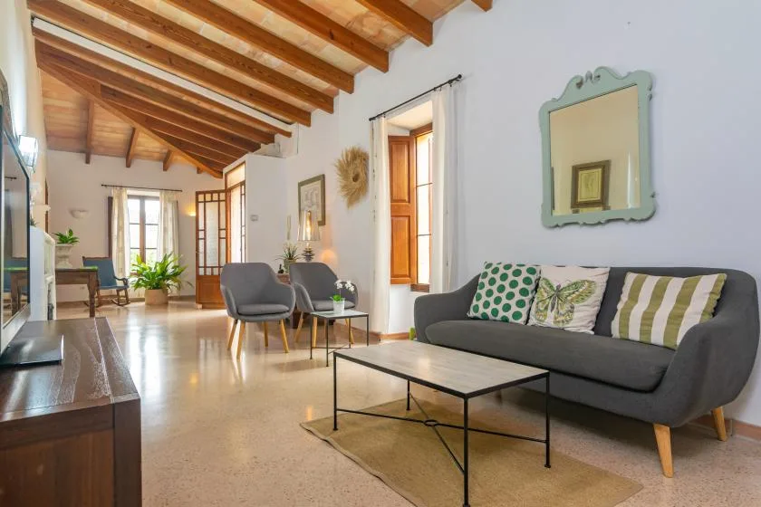 A bright living room with a gray sofa and wooden ceiling beams.