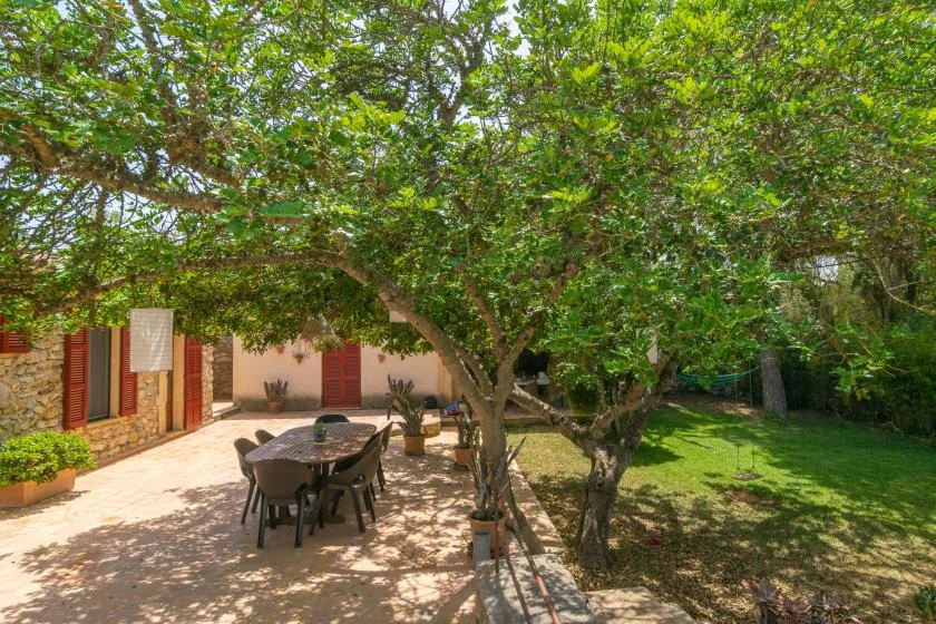 A shaded outdoor patio with a dining table beside a leafy garden.