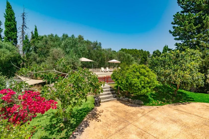 A landscaped garden path leads to a poolside seating area beneath umbrellas.