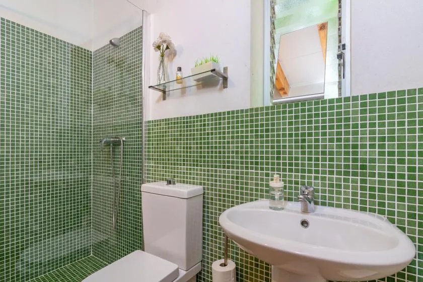 A bathroom with green tiled walls, a sink, and a toilet.