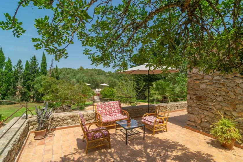 A sunny outdoor patio has seating, a small table, and views of green hills.