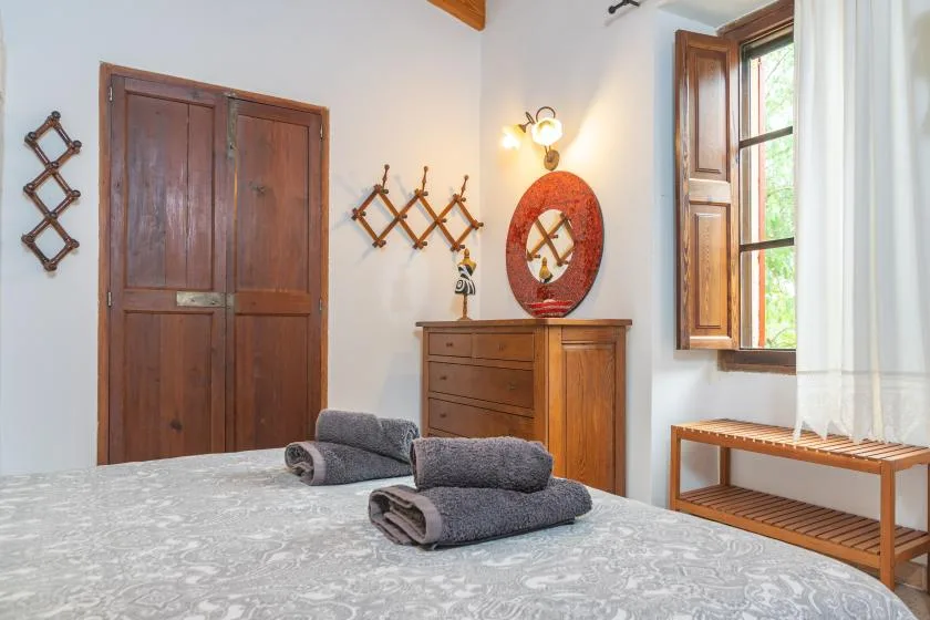 A bedroom with a wooden dresser, dark towels, and a window with open shutters.