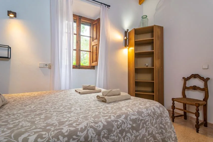 A bedroom with a patterned bedspread, a window, and a wooden shelving unit.