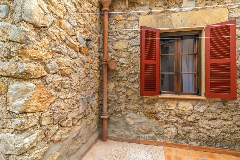 A stone exterior wall with a window framed by open red shutters.