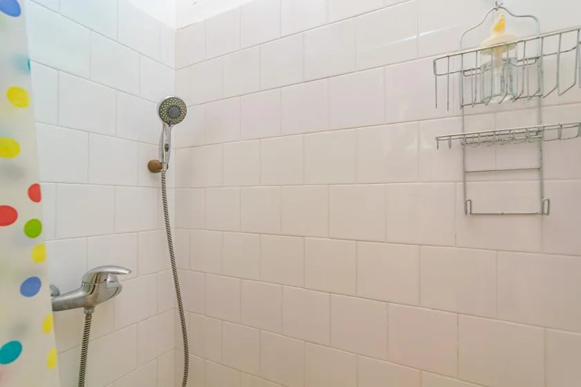 A tiled bathroom shower with a handheld showerhead and wall-mounted rack.