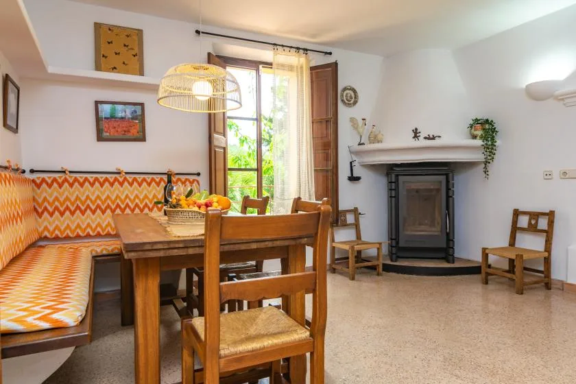 A dining and sitting area features a wooden table, patterned bench, and fireplace.