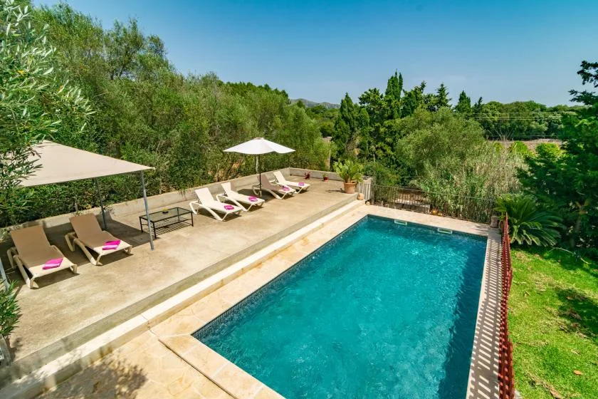 An outdoor swimming pool sits beside a paved deck with lounge seating and umbrellas.