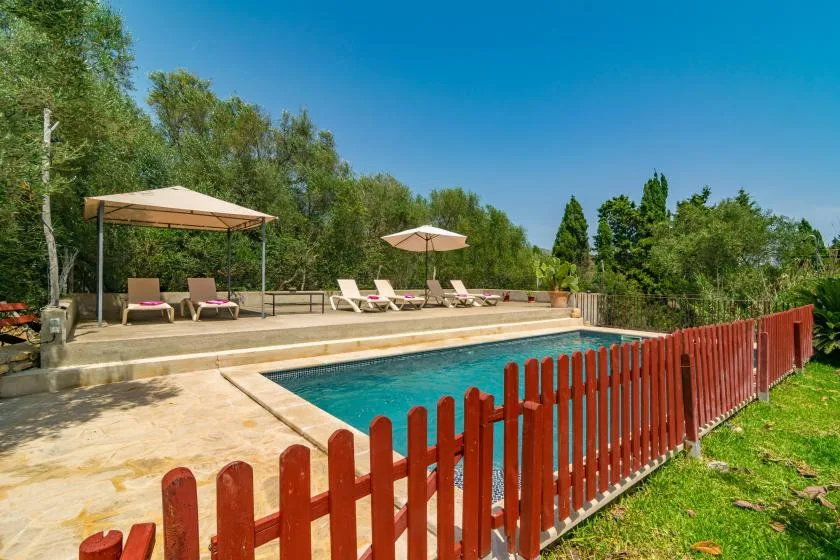 An outdoor swimming pool beside a patio with lounge seating and shade umbrellas.