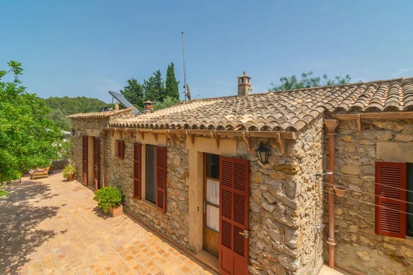 A stone house with terracotta roof tiles faces a sunny paved courtyard.