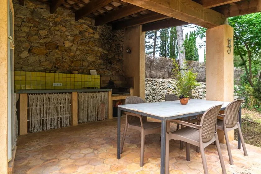 A covered outdoor dining area with a table and seating beside a stone wall.