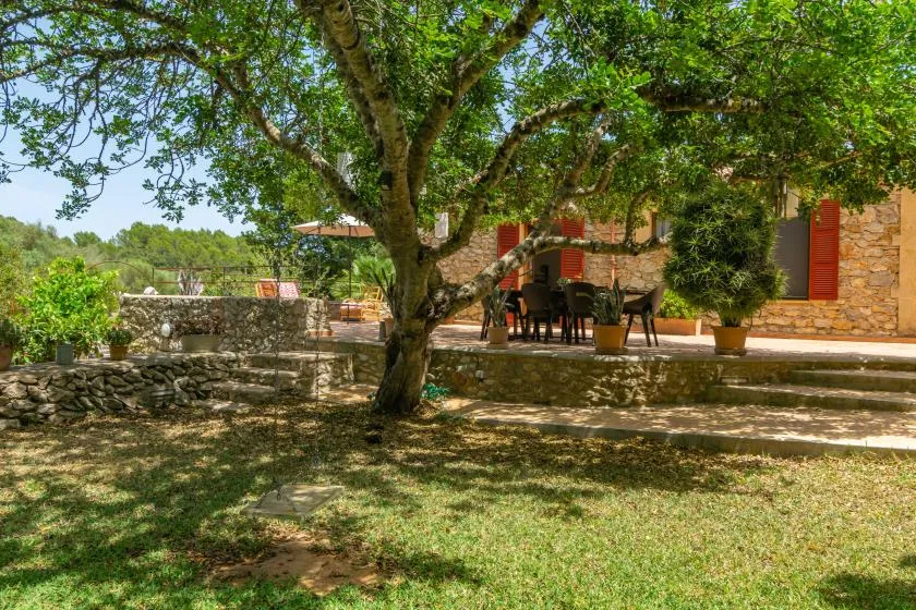 A shaded outdoor patio with seating beside a stone building.