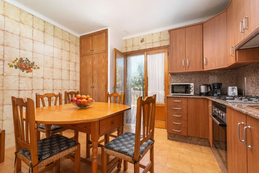 Un comedor con asientos de madera junto a una cocina y puertas de vidrio.