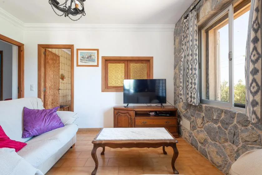 Una sala de estar con asientos, un televisor y una mesa de centro junto a una ventana grande.