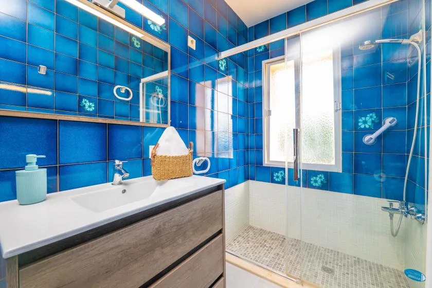 Un baño de azulejos azules con lavabo, mueble y ducha.