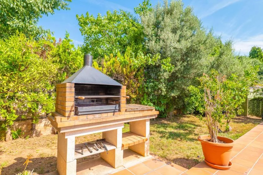 Una parrilla al aire libre está en un patio de baldosas rodeado de vegetación.