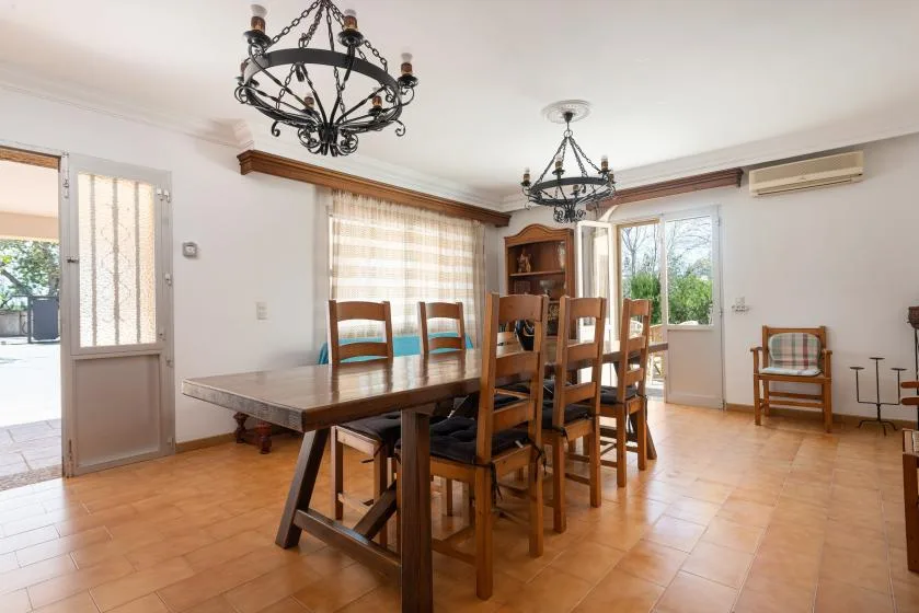 Un comedor con una larga mesa de madera y sillas bajo dos lámparas de araña.