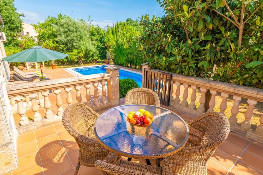 Un patio de baldosas con una mesa redonda de vidrio da a una piscina y vegetación.