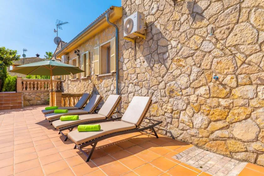 Una terraza soleada de piedra tiene tumbonas junto a la casa.