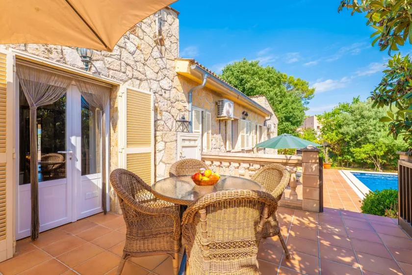Una casa de piedra da a un patio de baldosas con asientos de mimbre y una piscina.