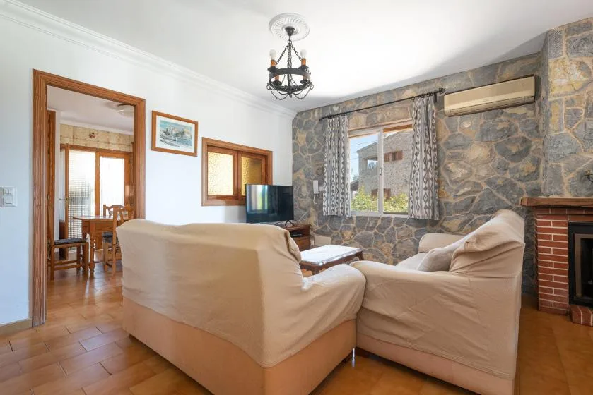 Una sala de estar con asientos beige, una pared de piedra y una ventana.