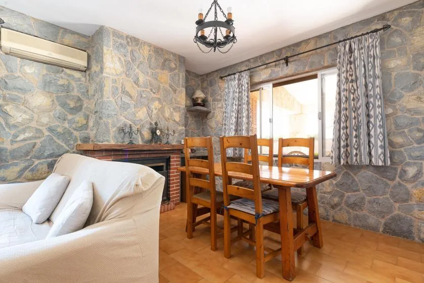 Una zona de estar y comedor con paredes de piedra, mesa y asientos de madera.