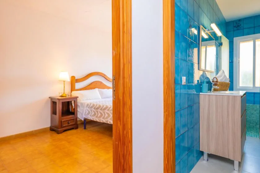 Un dormitorio junto a un baño con azulejos azules, separado por una puerta de madera.