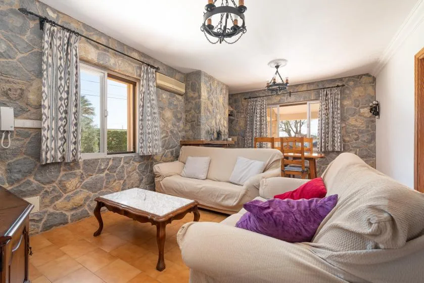 Sala de estar con paredes de piedra, asientos, una mesa de centro y un comedor.