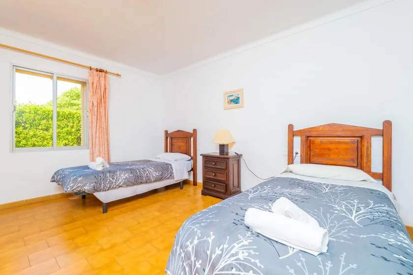 Un dormitorio con dos camas, ropa de cama estampada y una ventana con vista a la vegetación.