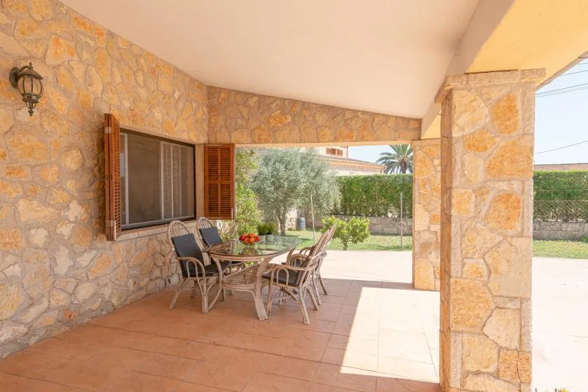 Un patio cubierto de piedra con asientos y una mesa al aire libre da a un jardín.