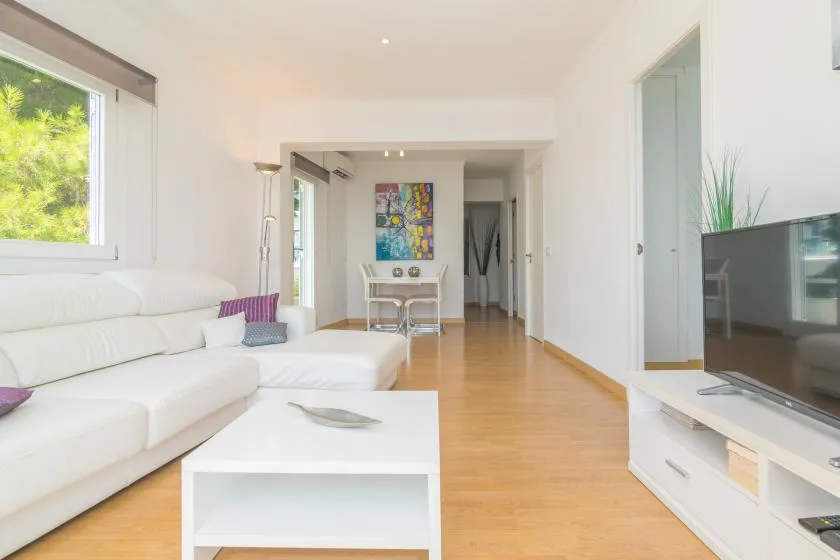 A bright living room with white seating, a coffee table, and a television.