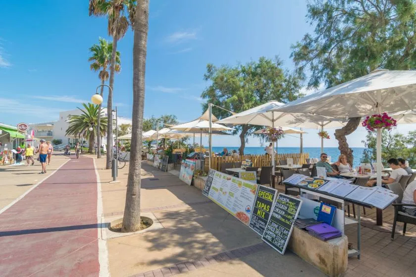 A seaside promenade with outdoor market stalls and shaded seating.