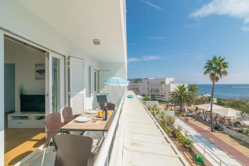 A balcony with outdoor seating overlooks palm trees and the sea.