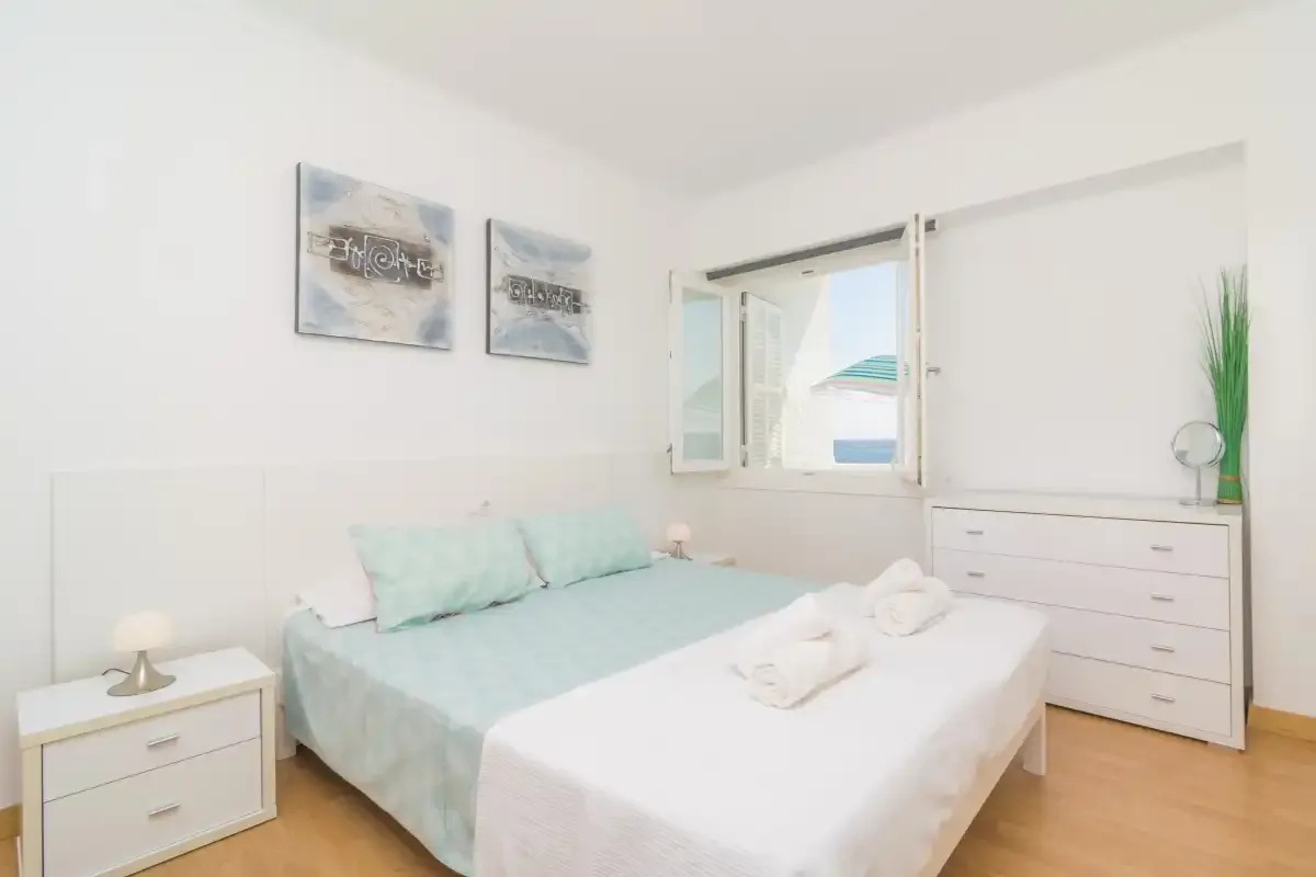 A bright bedroom with a bed, bedside table, and an open window.
