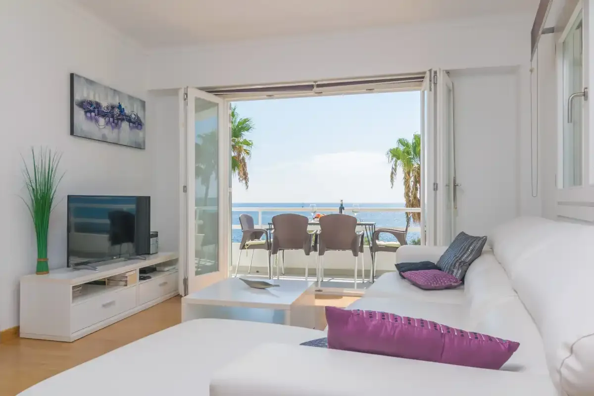 A bright living room opens onto a balcony with a view of the sea.