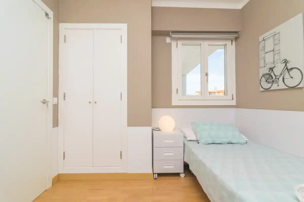 A bedroom with a single bed, bedside table, and window.