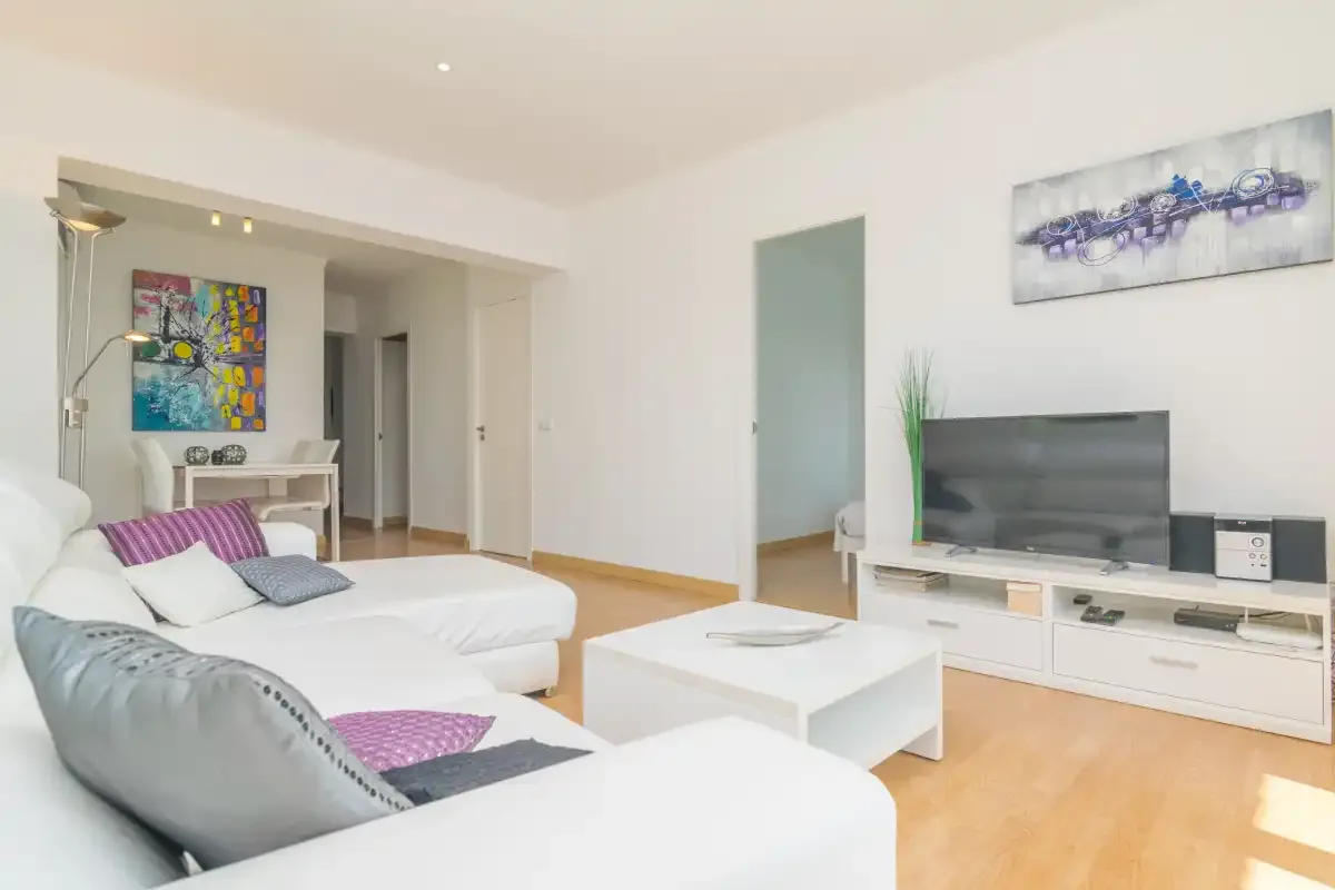 A bright living room with white seating, a coffee table, and a television.