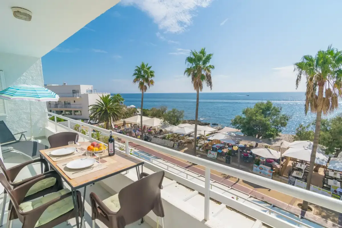A balcony dining area overlooks a palm-lined beach and the sea.