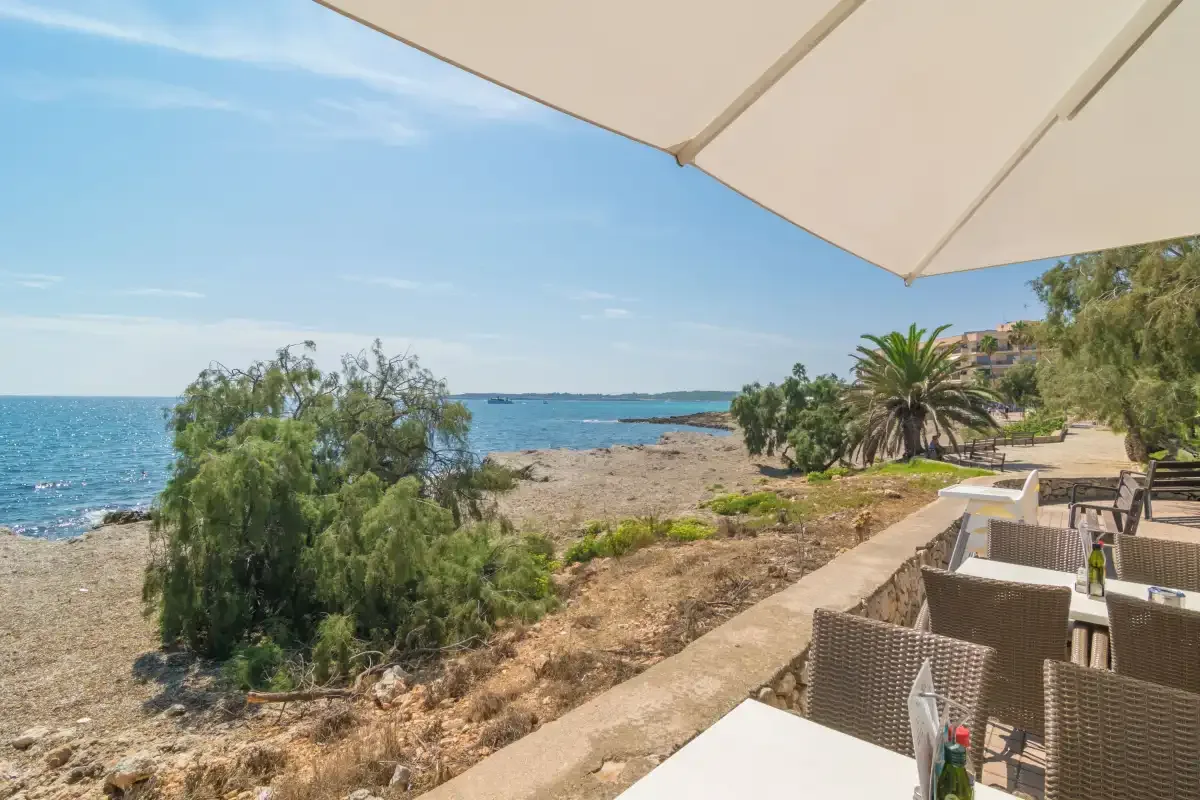 A seaside terrace overlooks a rocky shoreline beneath a large sunshade.