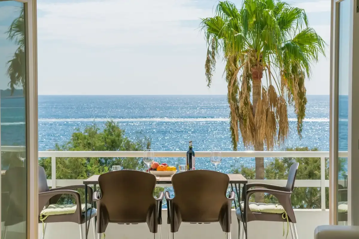 A balcony dining area overlooks the sea, with a palm tree beside the railing.