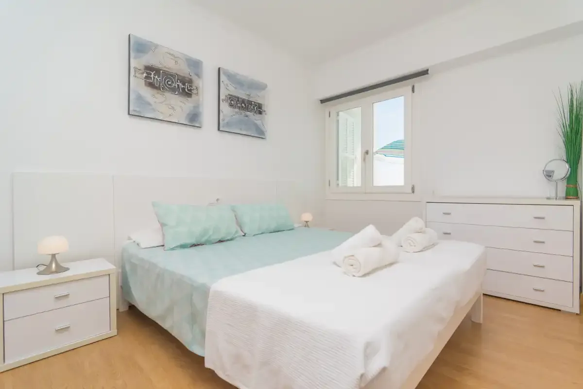 A bright bedroom with a bed, bedside tables, and a window.