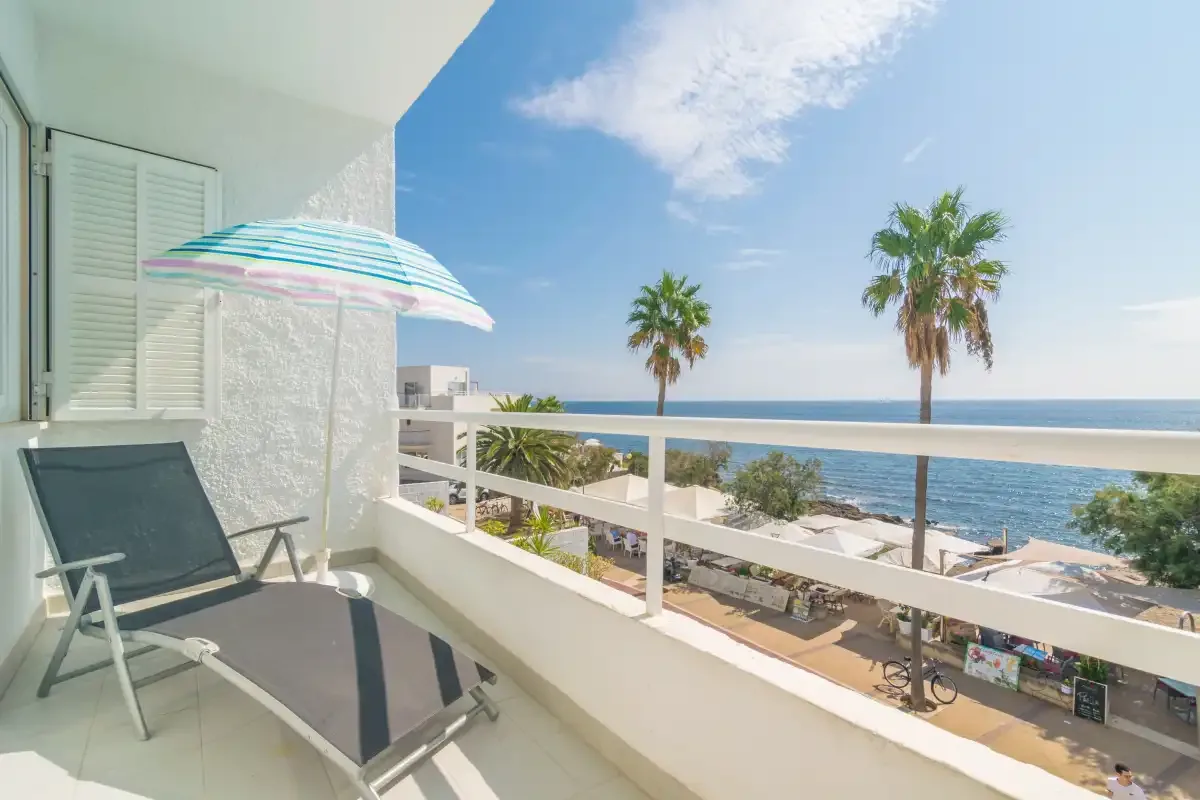 A balcony overlooks the beach and sea, with palm trees along the shore.