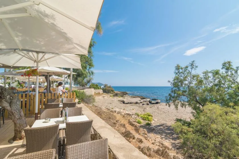 Outdoor dining area beside a rocky shoreline, with tables under large umbrellas.