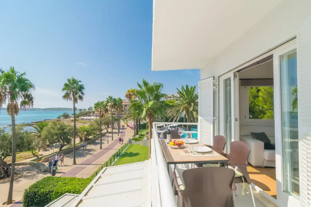 A balcony dining area overlooks a palm-lined seaside promenade.